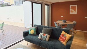 Una sala de estar moderna con un sofá verde oscuro, dos cojines, una mesa de comedor con sillas y un ventanal corredizo que da a un espacio exterior.