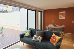 Een moderne woonkamer met een donkergroene bank, twee kussens, een eettafel met stoelen en een schuifpui naar een buitenruimte.