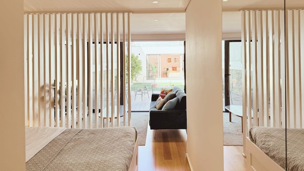 Un dormitorio moderno con dos camas, un sofá y un ventanal corredera que da a un patio.