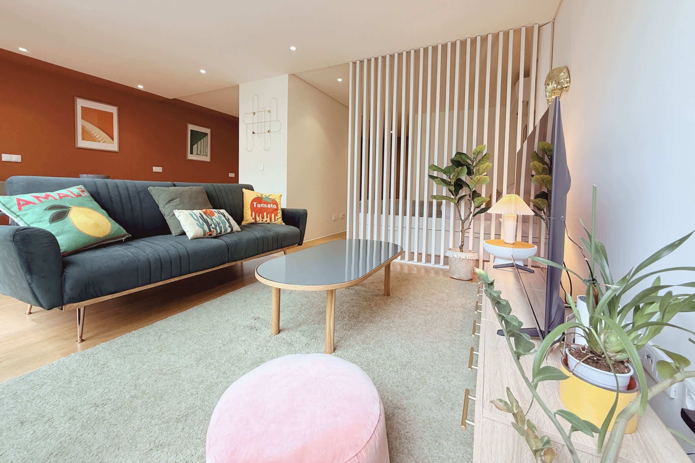 A living room with a dark green sofa, a round coffee table, a pink ottoman, and a striped partition.