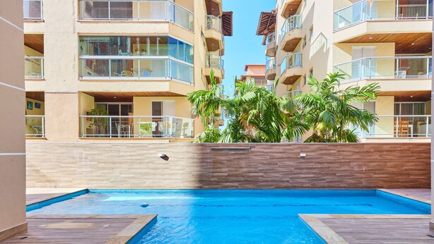 A swimming pool surrounded by a building with multiple balconies and a wooden wall. - Raridade 2 vagas Praia Grande - Nobre  (Ubatuba)