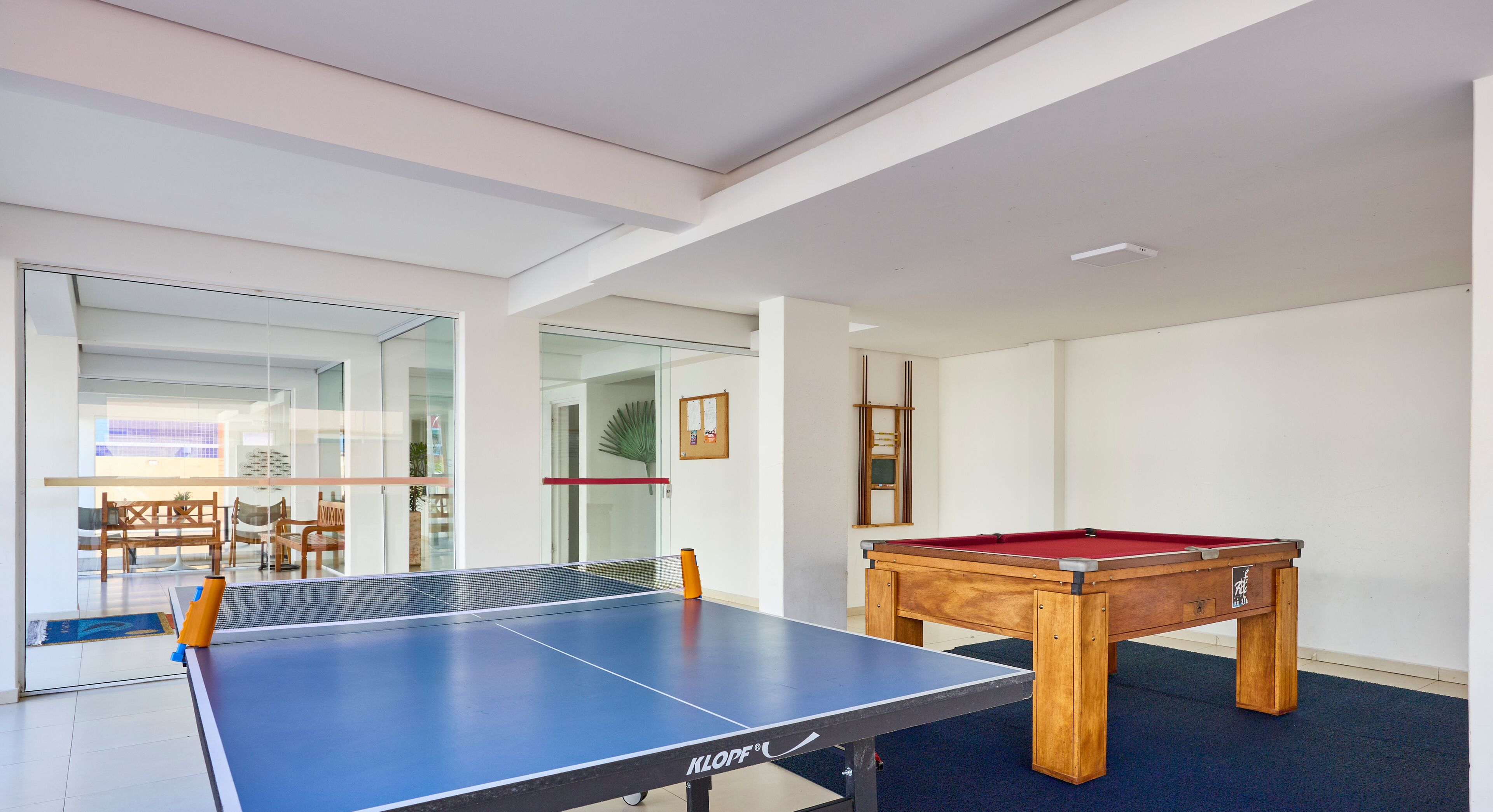 A room with a ping pong table, a pool table, and a glass door leading to an outdoor area with a view.