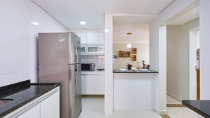 A modern kitchen with white cabinets, stainless steel appliances, and a black countertop. - Raridade 2 vagas Praia Grande - Nobre  (Ubatuba)