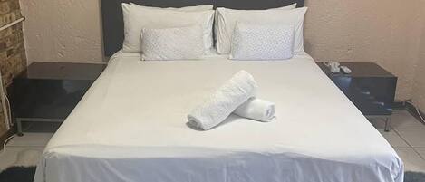 A neatly made bed with white linens and a rolled towel, a black headboard, and a small bedside table with a lamp.