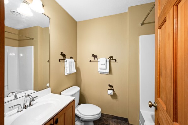 A bathroom with a sink, toilet, and mirror. There are towels hanging on hooks and a shower curtain.