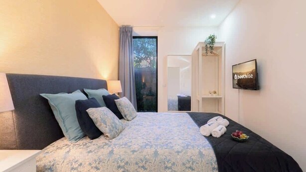 A modern hotel room with a large bed, a bedside table, a TV, and a view of the outdoors. - Charming Restful Flat w/ Terrace by HostWise (Porto)