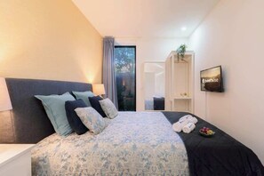 Une chambre d’hôtel moderne, dotée d’un grand lit, d’une table de chevet, d’une télévision et offrant une vue sur l’extérieur.