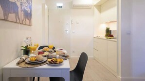 A dining area with a table set for breakfast, a kitchen area with a fruit bowl, and a painting on the wall. - Charming Restful Flat w/ Terrace by HostWise (Porto)