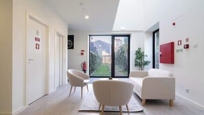 A modern living room with a sofa and armchairs, a large sliding glass door to a garden, and a fire extinguisher on the wall. - Charming Restful Flat w/ Terrace by HostWise (Porto)