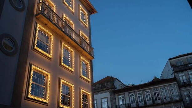 A building with multiple windows illuminated by warm lights, a balcony with railings, and a classic architectural style.