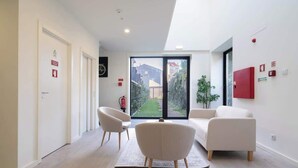 A modern hotel room with a large sliding glass door leading to a garden, a sofa, a chair, and a small table.