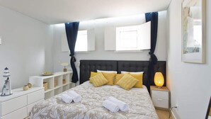 Quarto bem arrumado com uma cama grande, mesas de cabeceira, abajur e prateleira com objetos decorativos.