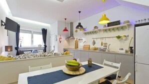 Uma cozinha moderna com armários brancos, uma mesa de jantar com toalha azul e diversos utensílios e eletrodomésticos.