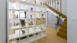 Um interior moderno com uma estante branca exibindo vários objetos, uma escada com degraus de madeira e uma pequena mesa com uma planta.