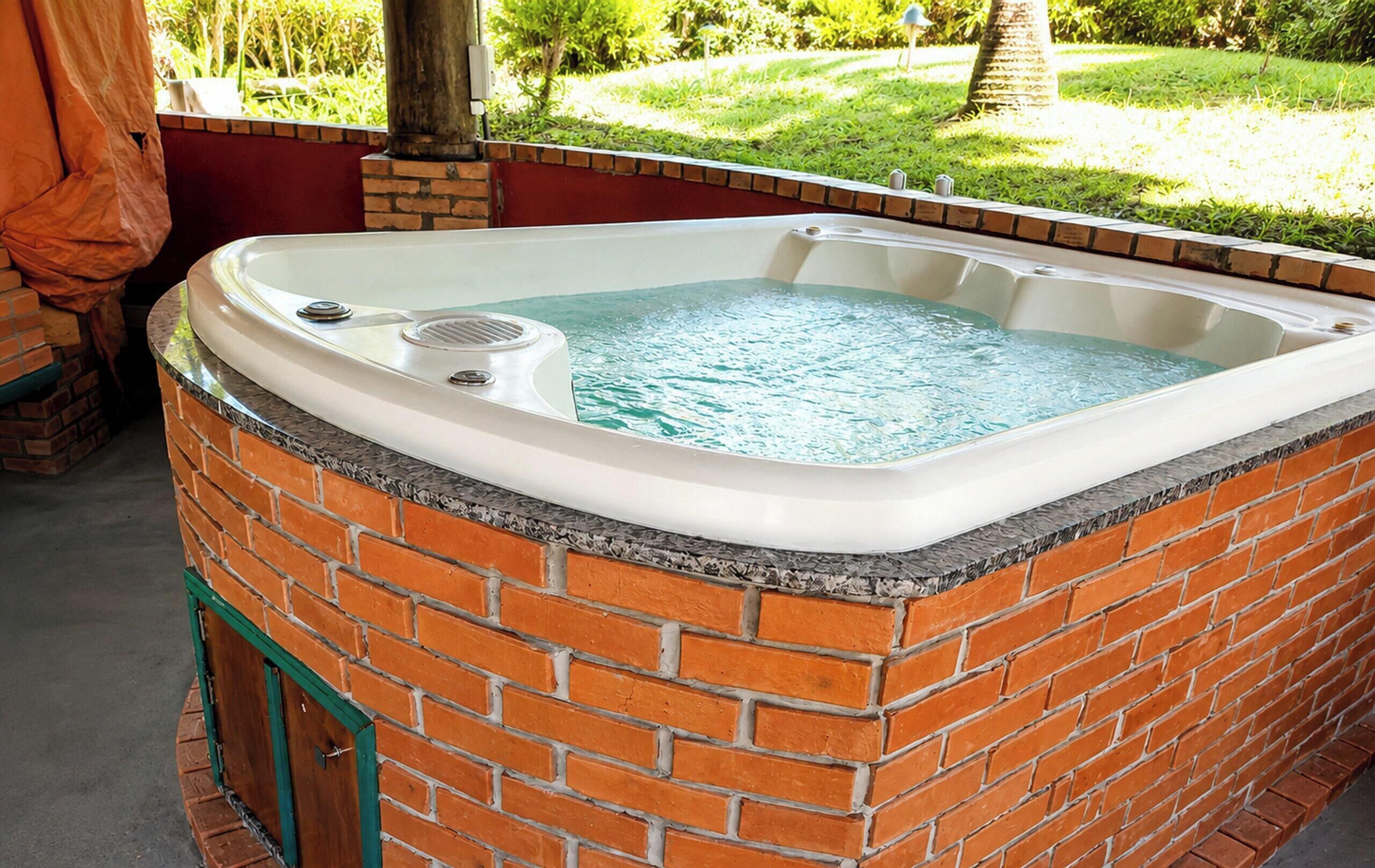 Uma banheira de hidromassagem com exterior em tijolo, cercada por um muro de tijolos e um espaço de varanda coberto.
