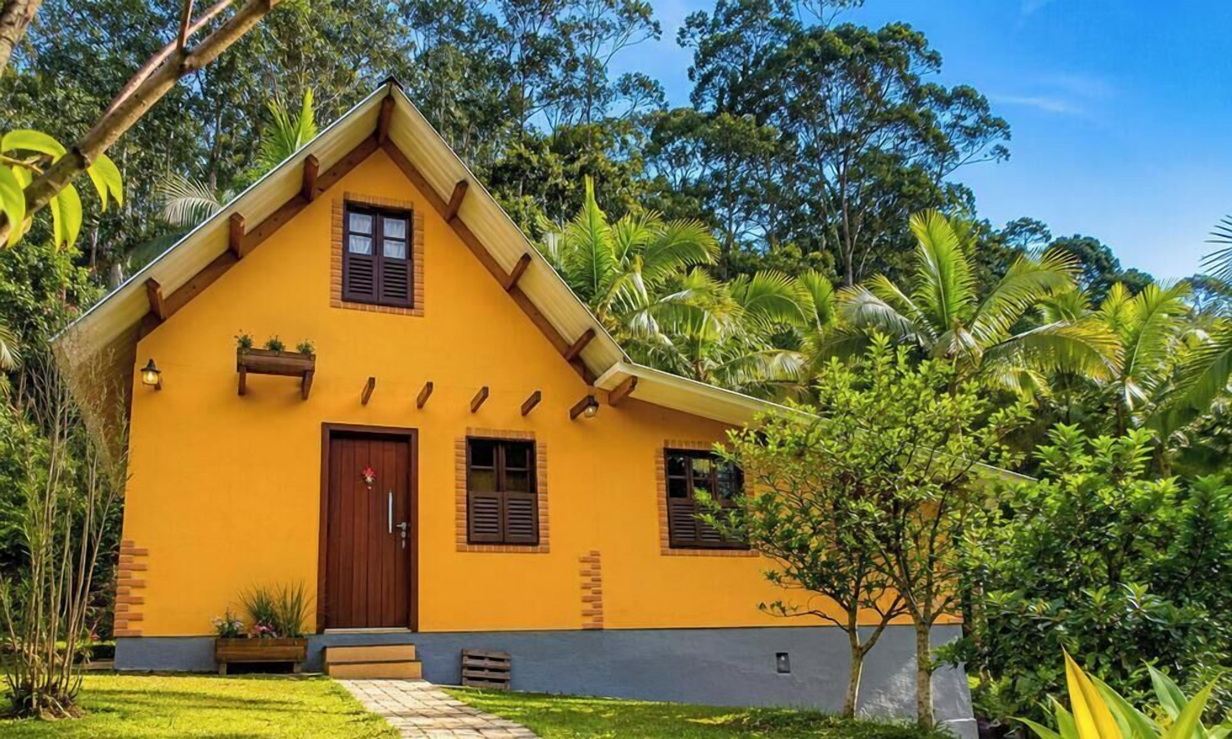 Una casa amarilla con puerta marrón, ventanas y un pequeño porche.