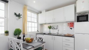 A modern kitchen with white cabinets, a microwave, and a sink. There is a dining table with chairs and a basket of fruit.