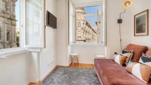 A cozy room with a red sofa, a window with a view of a street, and a small stool.