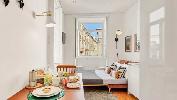 A compact room with a dining area, a bed, and a window providing a city view.