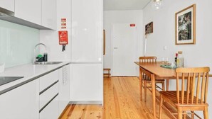 A modern kitchen with white cabinets, a wooden dining table with chairs, and a hanging light fixture.