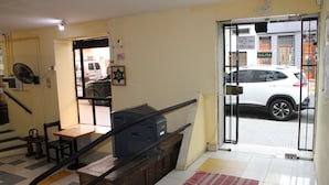 A hotel lobby with a reception desk, a fan, a staircase, and a view of the street outside. - Mitre Suites Hotel (Buenos Aires)