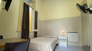 A room with a bed, a desk, a chair, a window with curtains, a bedside lamp, and a wall-mounted fan. - Mitre Suites Hotel (Buenos Aires)