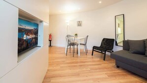 Un salon moderne comprenant un canapé, une table à manger avec des chaises, un téléviseur à écran plat fixé au mur et une petite table sur laquelle est posée une plante.