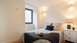 Une chambre à coucher avec un lit, une table de chevet, une lampe et une fenêtre.
