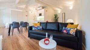 Un salon moderne avec un canapé en cuir noir, une table à manger avec des chaises et une petite table blanche sur laquelle se trouvent une bouteille et un verre.