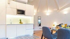 Una cocina moderna con armarios blancos, un microondas y un lavamanos. Hay una zona de comedor con dos sillas y una mesa lista para el desayuno.