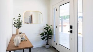 A hallway with a wooden table, two potted plants, a mirror, and a door leading outside. - Modern Joshua Tree Village Home (Joshua Tree)