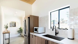 A modern kitchen with wooden cabinets, a stainless steel refrigerator, a microwave, and a sink. - Modern Joshua Tree Village Home (Joshua Tree)
