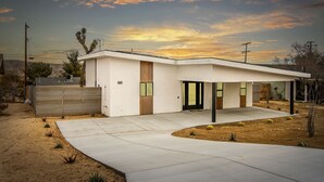 A modern single-story house with a covered patio, a garage, and a desert landscape in the background. - Modern Joshua Tree Village Home (Joshua Tree)