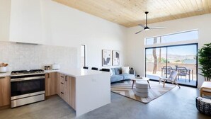 A modern kitchen with a central island, wooden cabinets, and a large window overlooking a scenic view. - Modern Joshua Tree Village Home (Joshua Tree)