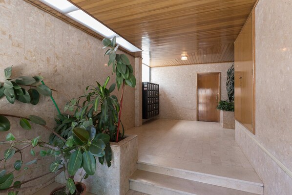 Amplio espacio interior con techo de madera, una escalera que conduce a una puerta y plantas en macetas.
