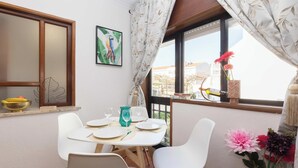 A dining area with a table set for four, a window with curtains, a painting, and a vase with flowers.