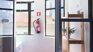 A hotel room with a washing machine, a fire extinguisher, and a wooden chair by the window.