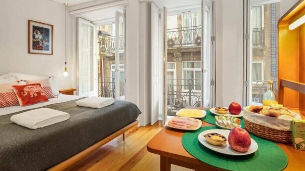 Habitación de hotel con cama, mesa de desayuno con platos de comida y vistas a un balcón con mobiliario exterior.