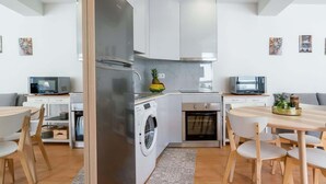 Une cuisine moderne avec des meubles blancs, un réfrigérateur en acier inoxydable, un lave-linge et un four à micro-ondes. Il y a également un coin repas avec une table et des chaises.
