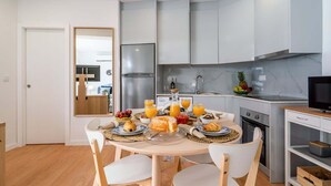 Une cuisine moderne avec un coin repas, comprenant une table ronde sur laquelle sont disposés des assiettes de nourriture et des boissons, ainsi qu’un téléviseur posé sur un meuble.