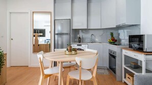 Une cuisine moderne avec des meubles gris, un réfrigérateur en acier inoxydable, un four à micro-ondes et un coin repas comprenant une table en bois et des chaises blanches.