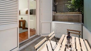 A small patio with a wooden table and chairs, a bottle of wine, and a glass.