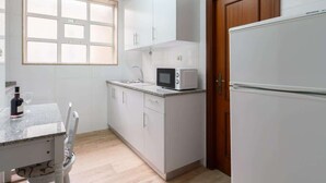 A compact kitchen with white cabinets, a microwave, a refrigerator, a window, and a dining area with a table and chairs.