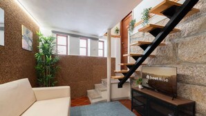 A modern living room with a sofa, a TV on a stand, a staircase with wooden shelves, and a plant.