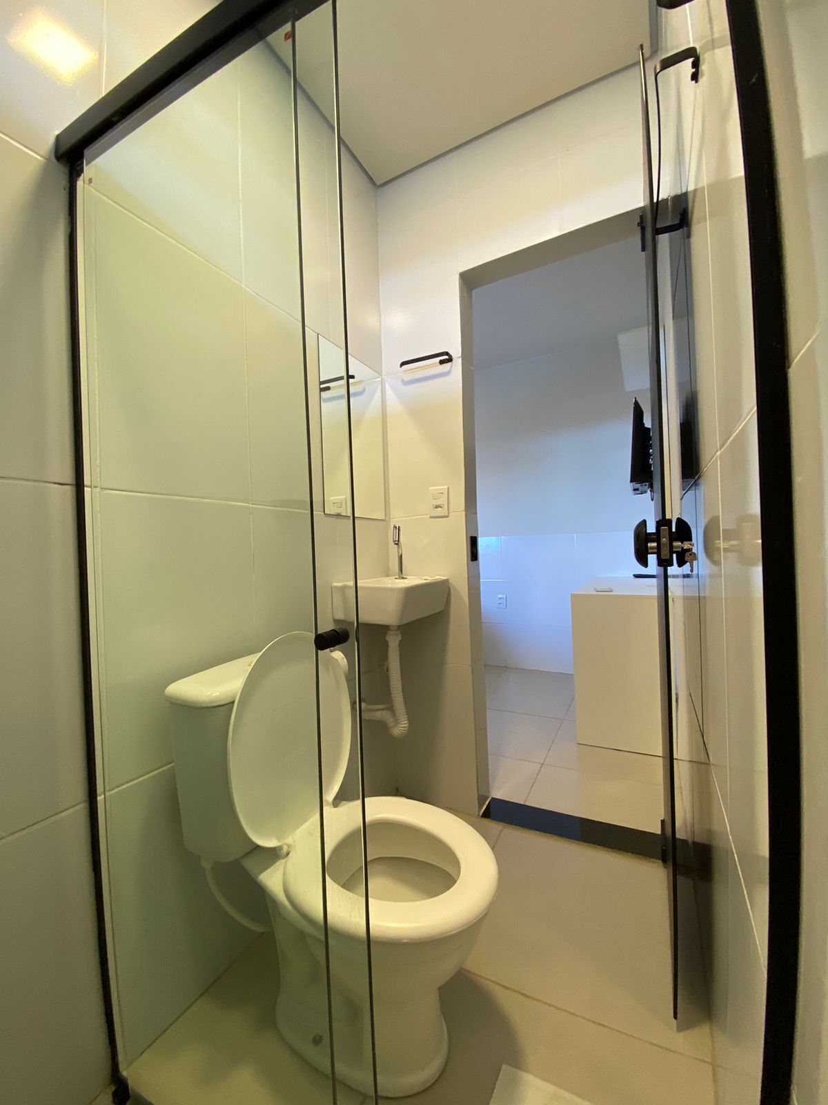 Une salle de bain moderne avec une paroi de séparation en verre, des toilettes blanches, un lavabo et un miroir.