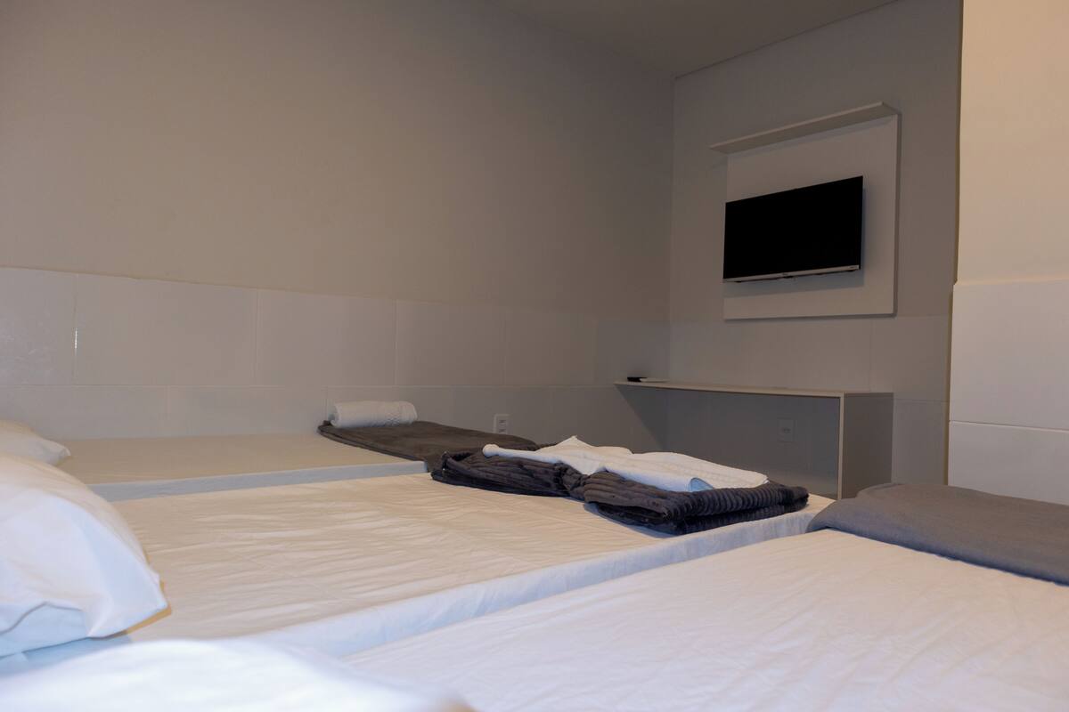 Ein Hotelzimmer mit zwei Einzelbetten, einem flachbildfernseher an der Wand und einem kleinen Nachttisch.