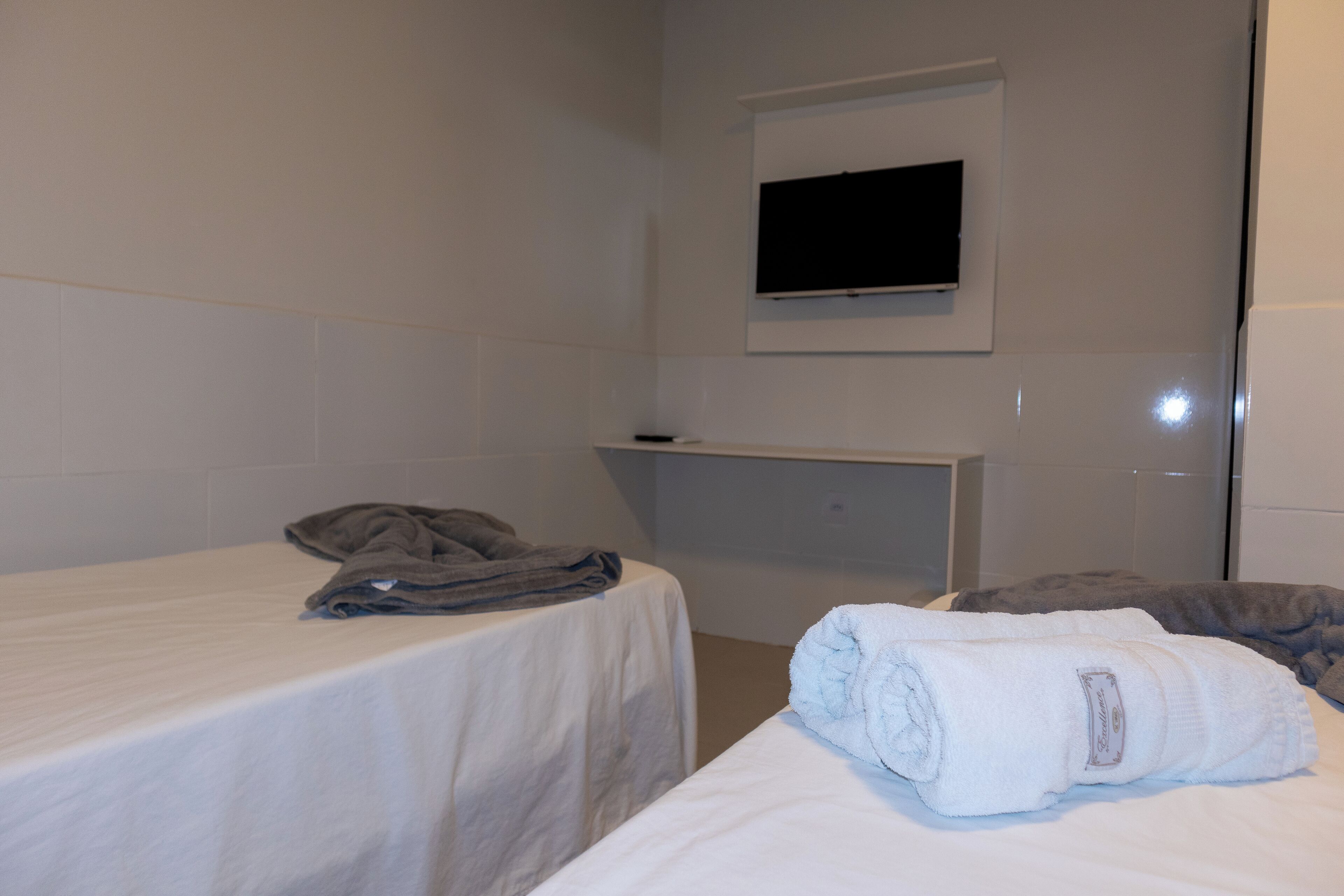 Habitación de hotel con dos camas, un televisor de pantalla plana montado en la pared y un estante pequeño.