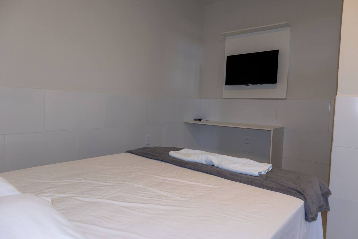 Ein Hotelzimmer mit einem Bett, einem an der Wand befestigten Flachbildfernseher und einem kleinen Regal darüber.