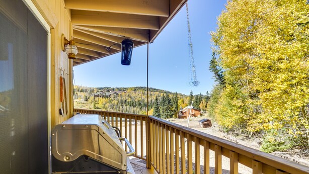 A wooden deck with a grill, a hanging lantern, and a view of a forested hillside. - Cozy Condo w/ Fireplace - Near Brian Head Resort! (Brian Head)