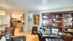 A living room with a sofa, a coffee table, and a bookshelf. There is a dining table with chairs and a kitchen in the background. - Cozy Condo w/ Fireplace - Near Brian Head Resort! (Brian Head)